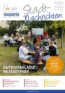 Eine Gruppe von Studenten sitzt auf Bänken in einem Park und benutzt Laptops. Einige sitzen auf dem Gras, andere stehen herum.