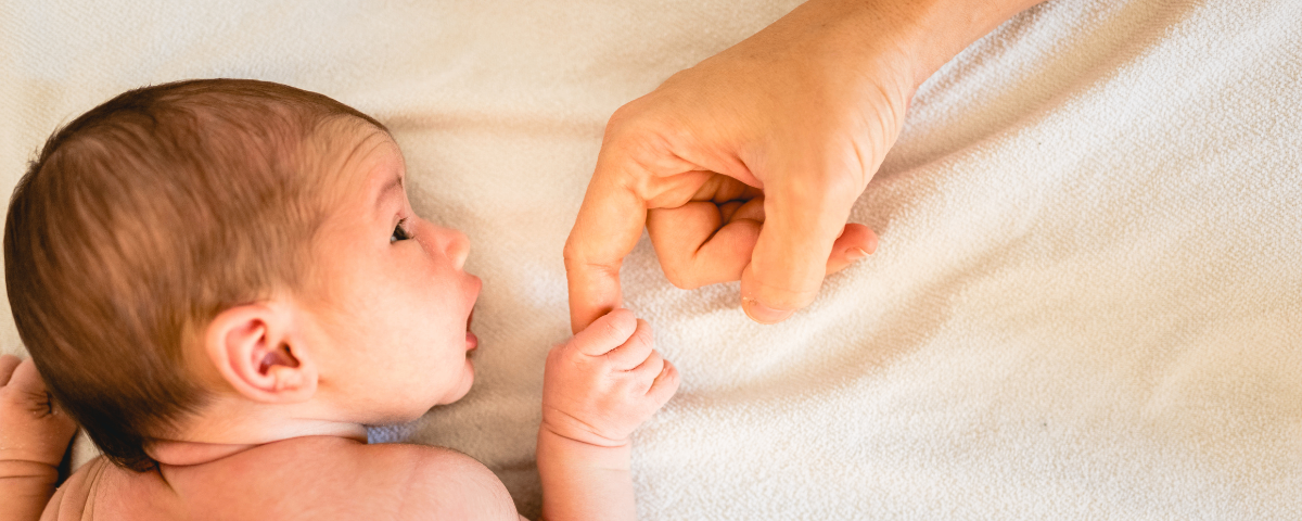 Eine Hand berührt den Finger eines Neugeborenen und konzentriert sich auf die Interaktion zwischen dem Erwachsenen und dem Baby.