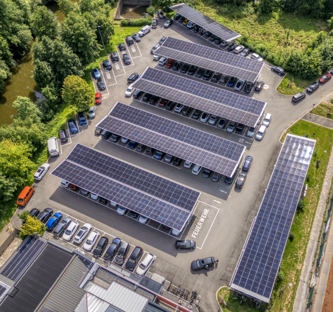Luftaufnahme eines Parkplatzes mit Solarpanelen auf den Dächern der geparkten Autos. Der Parkplatz ist gut organisiert, mit Reihen von Autos und Solarpanelen.