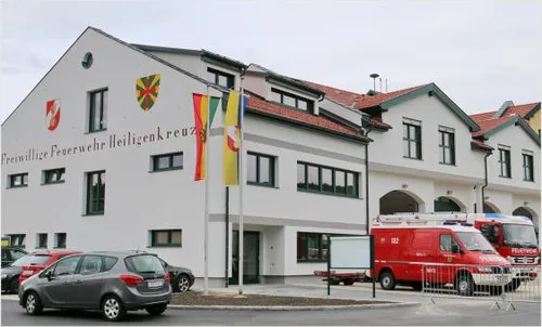 Die Vorderseite eines weißen Gebäudes mit roten Dächern. Vor dem Gebäude hängen Fahnen und vor dem Gebäude sind Rettungsfahrzeuge geparkt.