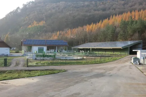 Ein ländliches Gebiet mit zwei Solaranlagen, einem Grasfeld und einem Berg im Hintergrund.