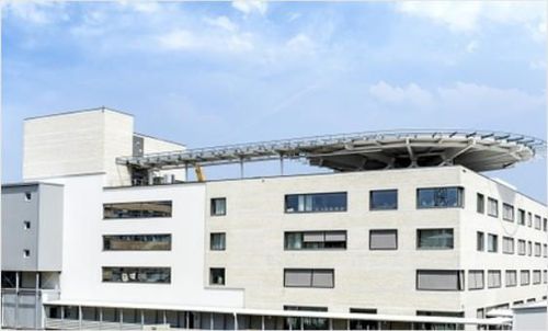 Ein modernes weißes Gebäude mit Glasfenstern und einem gebogenen Dach auf der Oberseite unter einem blauen Himmel mit Wolken.
