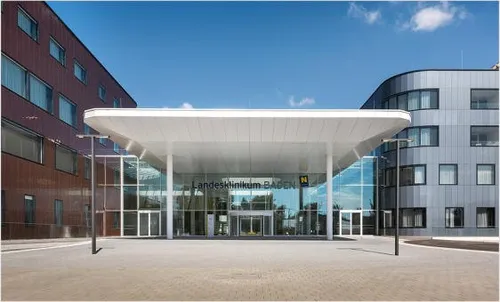 Der Eingang eines modernen Krankenhausgebäudes mit einem großen Vordach und Glaswänden. Das Gebäude ist mit 'Landesklinikum BADEN' beschriftet.