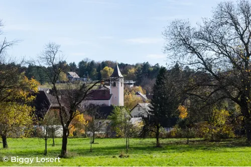 Ein Blick auf ein Dorf mit Bäumen und einem Turm, unter einem klaren Himmel, im Herbst.