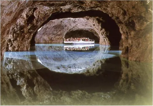 Ein Boot mit Passagieren fährt durch eine Höhle mit einer Wasserreflexion.