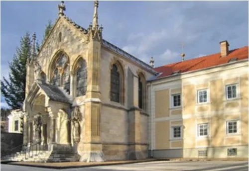 Eine alte Kirche mit einem roten Dach, mehreren Bogenfenstern und zwei Statuen steht unter einem bewölkten Himmel.
