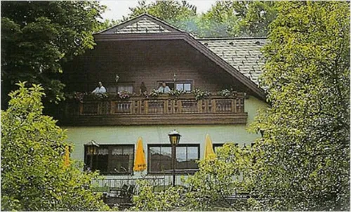 Ein zweistöckiges Haus mit Balkon hat zwei Personen darauf. Es hat gelbe Regenschirme und Straßenlaternen davor.