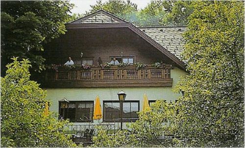 Ein zweistöckiges Haus mit Balkon hat zwei Personen darauf. Es hat gelbe Regenschirme und Straßenlaternen davor.