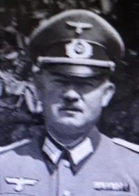 Ein älterer Mann in einer Militäruniform mit Abzeichen steht draußen und sieht geradeaus.