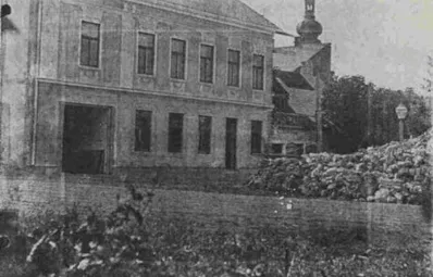 Ein Schwarz-Weiß-Foto eines alten Gebäudes mit mehreren Fenstern und einem Turm im Hintergrund.