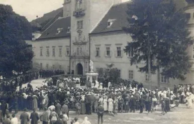 Ein altes Foto zeigt eine Menschenmenge vor einem Gebäude mit einer Statue in der Mitte.