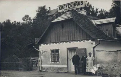 Schwarz-Weiß-Foto zeigt drei Personen vor einem kleinen Gebäude mit dem Schild Kaffeehaus.