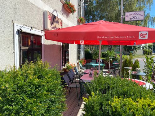 Eine Außensitzecke eines Cafés mit einem roten Regenschirm, einem Schild mit der Aufschrift Cafe Salon und Tischen und Stühlen.