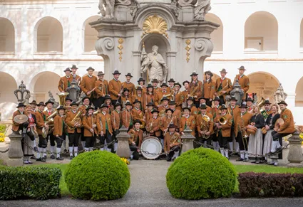 Eine Gruppe von Musikern in traditionellen Kostümen posiert für ein Foto vor einem historischen Gebäude mit Bogenstrukturen und einer Statue.