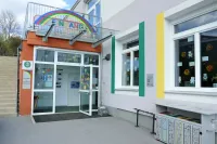 Der Eingang eines Gebäudes mit einer Glastür und Balkon. Ein bunter Regenbogen-Schild ist über dem Eingang, und ein Rauchverbotsschild ist an der Wand.