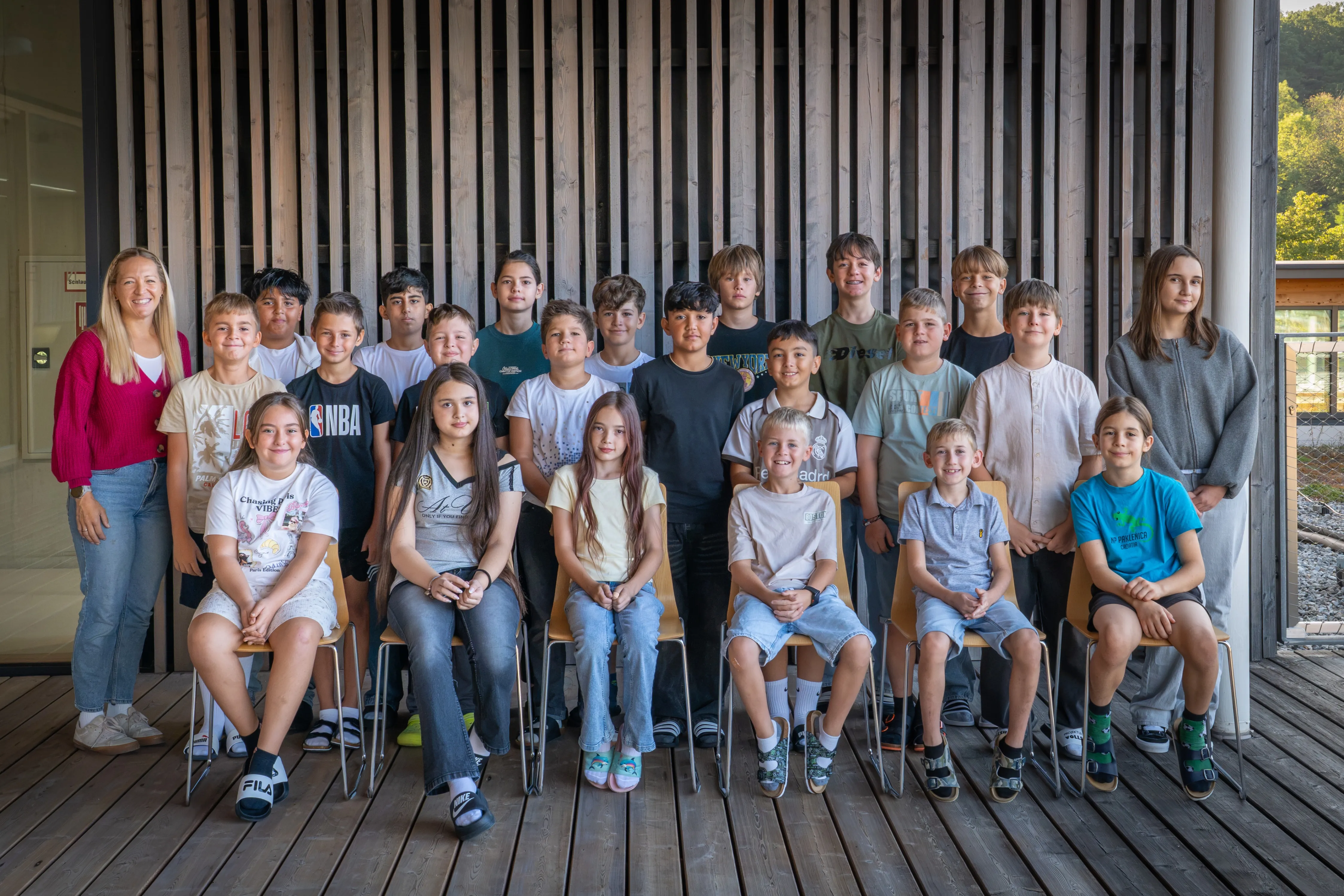 Eine Gruppe von Kindern und Jugendlichen posiert für ein Foto in einem Raum mit Holzwänden. Einige sitzen auf Stühlen, andere stehen.