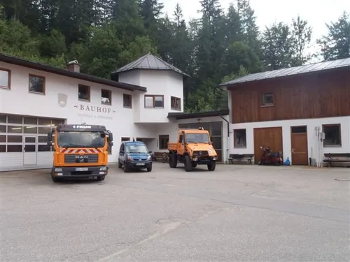 Ein Gebäude mit dem Namen Bauhof davor hat zwei Lastwagen, ein Auto und einen Motorrad vor sich geparkt.