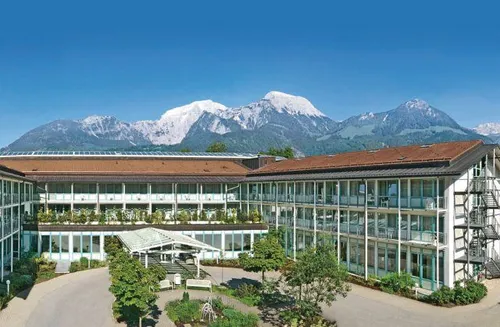 Ein modernes Hotelgebäude befindet sich in einer ruhigen Umgebung mit üppiger Grünfläche und einer Bergkette im Hintergrund.
