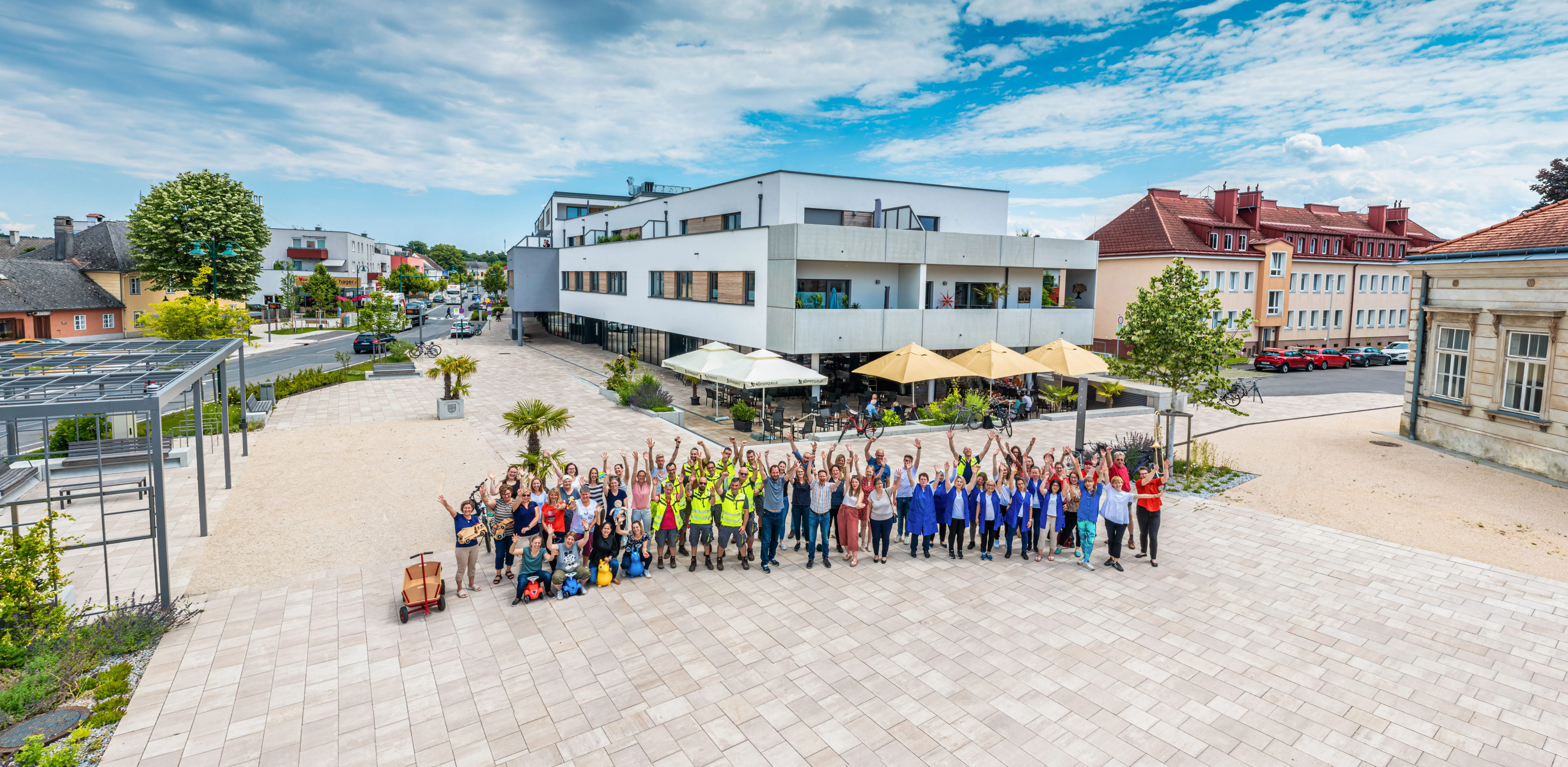 Eine große Gruppe von Menschen in passenden blauen Uniformen posiert vor einem modernen Gebäude an einem sonnigen Tag.