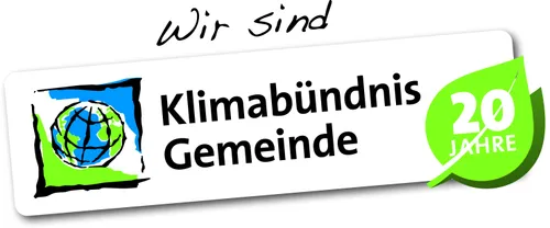 Ein weißer Schild mit fetter schwarzer Schrift lautet 'Wir sind Klimabündnis Gemeinde'. Es scheint sich um eine Erklärung oder ein Motto zu handeln.
