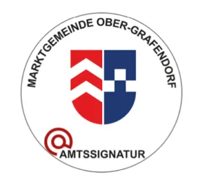 Das Bild zeigt ein kreisförmiges Logo mit einem Schild, der ein rotes und blaues Design, einen stilisierten Buchstaben 'S' und den Text 'Marktgemeinde Ober-Grafendorf' enthält. Unter dem Schild steht der Text 'Amtssiegel'.