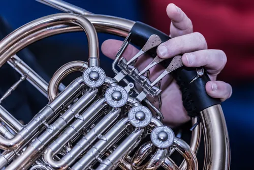 Die Hände einer Person justieren ein französisches Horn mit schwarzem Griff. Das französische Horn hat glänzende Silber- und Messingteile und komplizierte Designs.