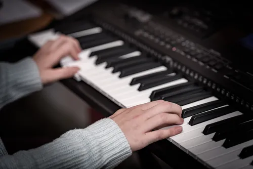Eine Person in einem Pullover spielt ein digitales Klavier mit den Händen auf den Tasten. Das Klavier hat eine Mischung aus schwarzen und weißen Tasten.