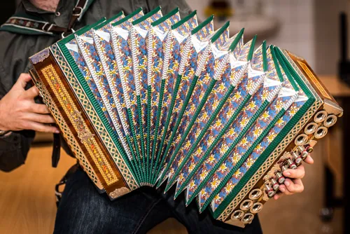 Eine Person hält ein Akkordeon mit einem blau-weißen Blumendesign. Das Instrument hat einen Holzkörper und Metallverzierungen mit grünen Akzenten.