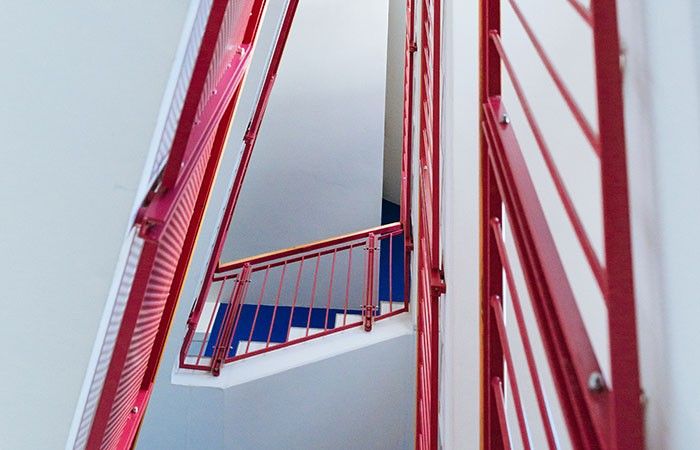 Ein Blick auf eine Treppe mit roten Geländern und blauen Stufen. Die Wände sind weiß mit roten Fensterläden.
