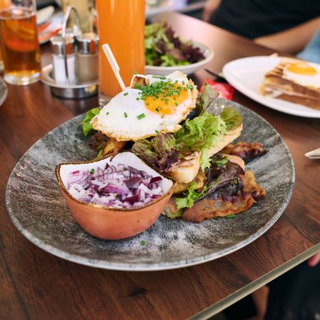 Ein Teller mit einem Frühstückssandwich, roten Zwiebeln und einem Getränk auf einem Tisch.