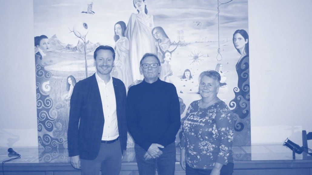 Drei Personen stehen gemeinsam vor einem Wandbild mit verschiedenen Frauen, Bergen und einem vom Himmel hängenden Seil.