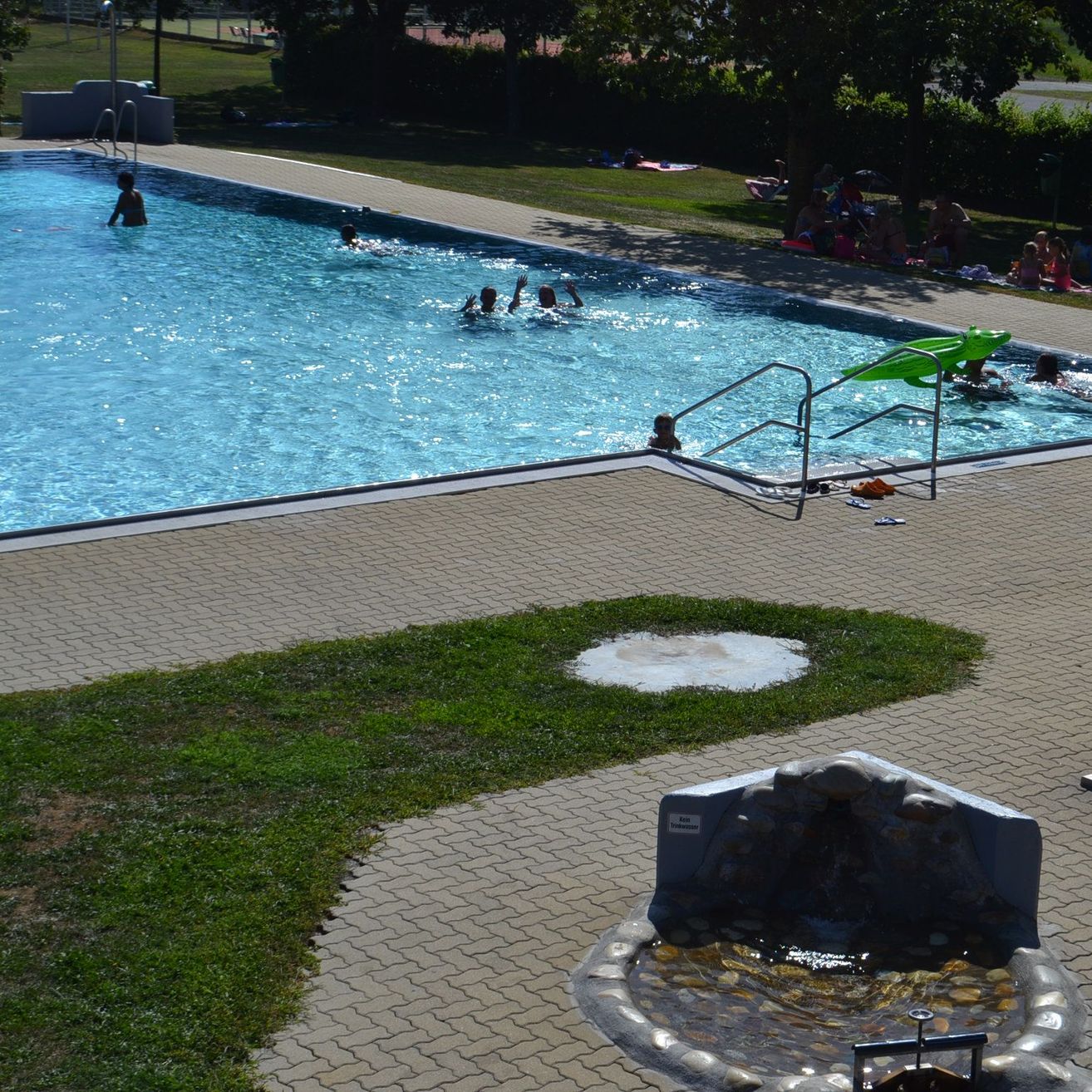 Ein Luftbild eines Freischwimmbads mit Schwimmenden und einer Frau, die sich neben dem Pool befindet.