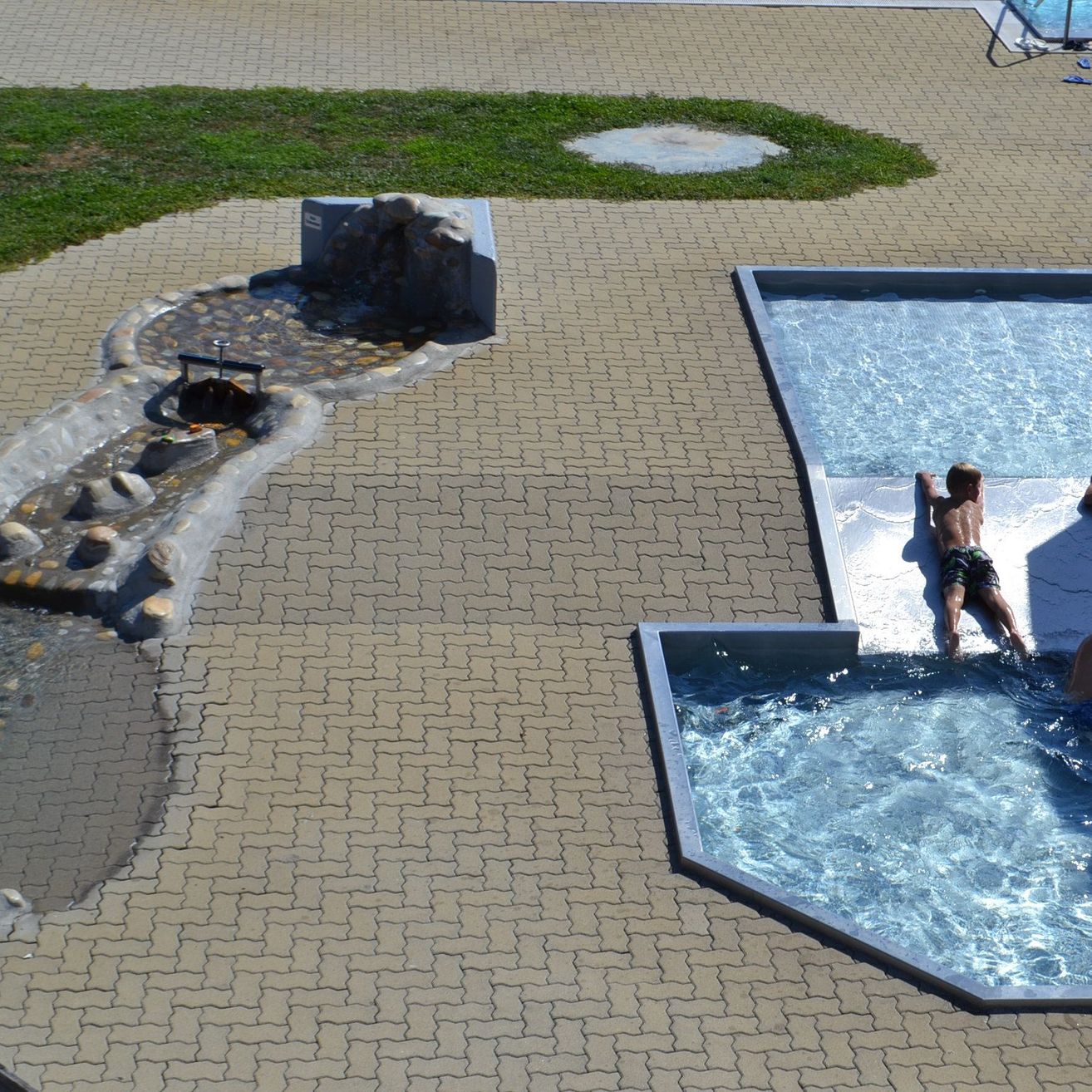 Luftaufnahme eines Schwimmbadkomplexes mit Wasserspielen und schwimmenden Kindern.