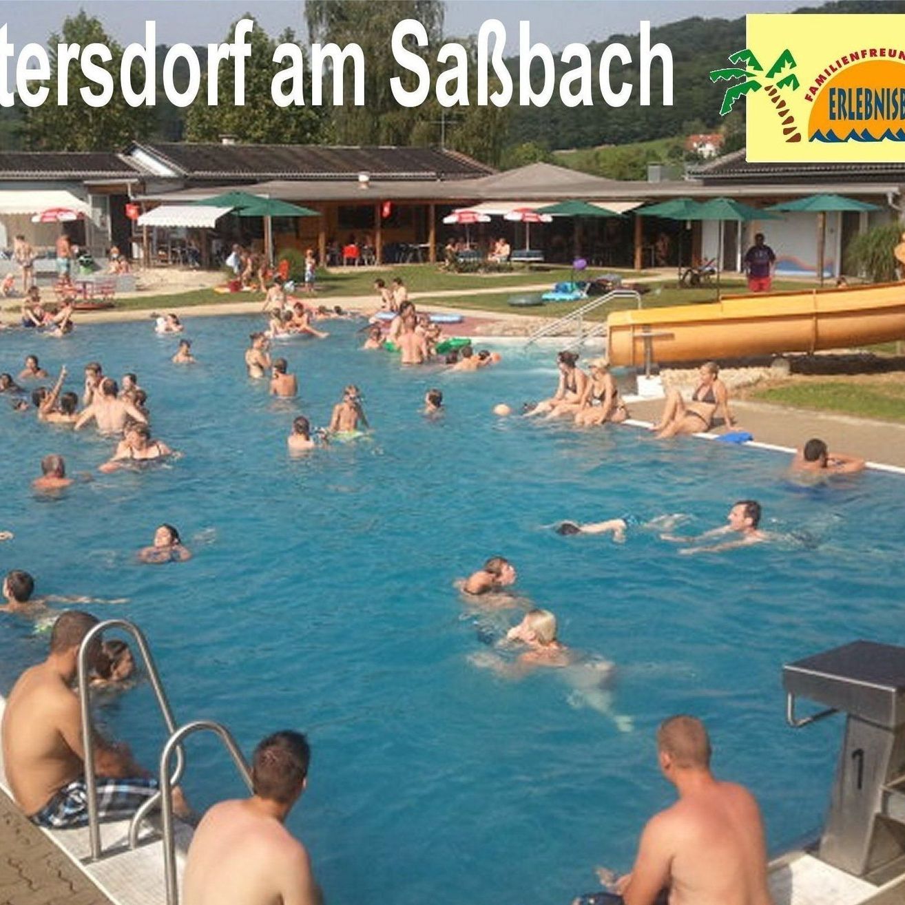 Ein großer Swimmingpool mit Schwimmenden und einer Wasserrutsche im Hintergrund. Der Text lautet 'Mettersdorf am Saisbach' und ein Logo.
