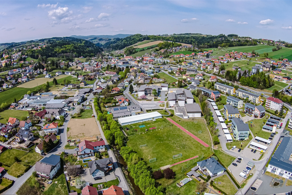 Abschnitt Bild: Luftaufnahme einer Stadt mit vielen Häusern und Gebäuden, grünen Feldern und einem blauen Himmel mit einigen Wolken.