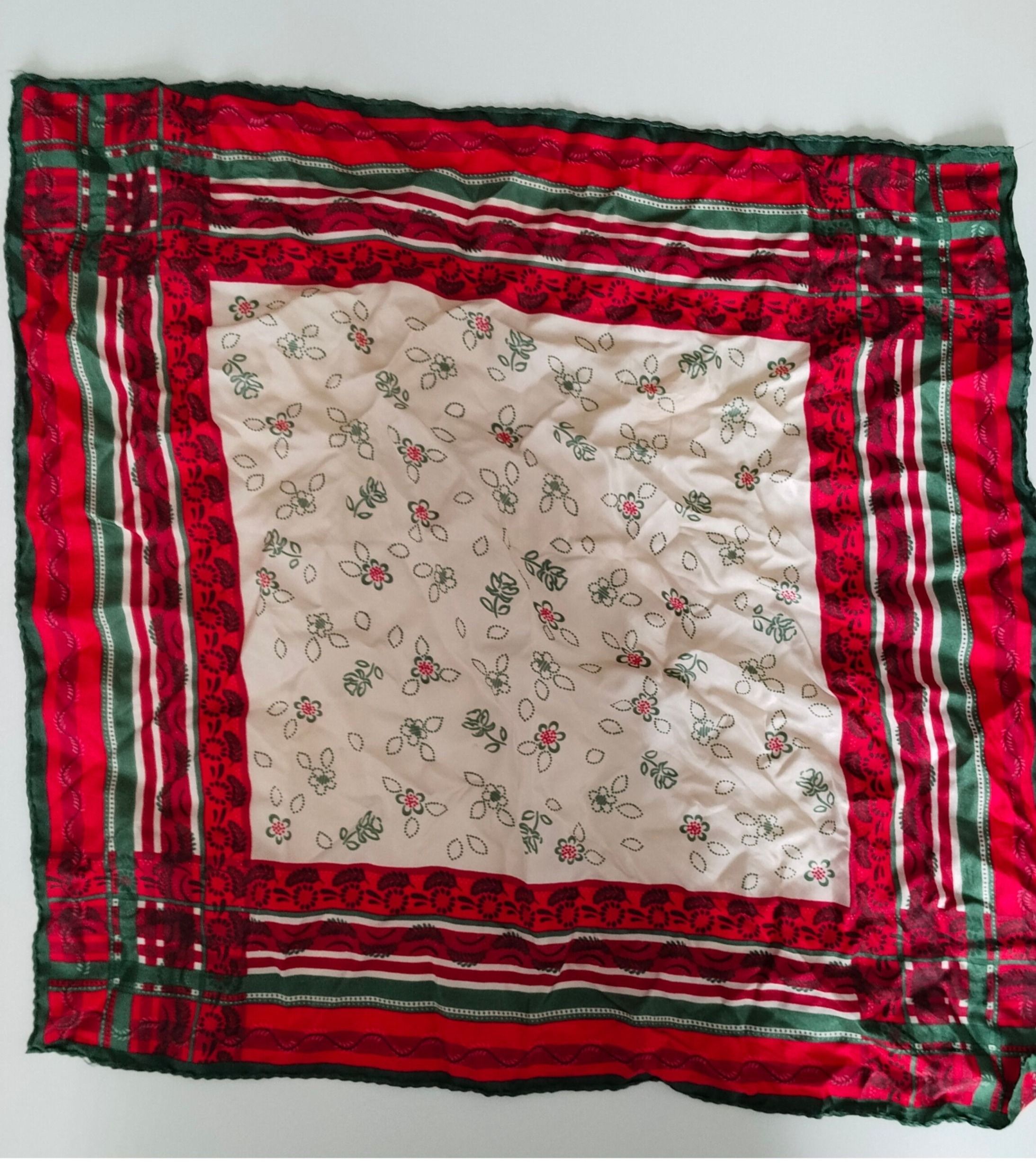 Ein rotes und grünes gestepptes Quadrat mit Blumenmustern auf weißem Hintergrund. Die Kanten sind mit roten und grünen Streifen eingefasst.