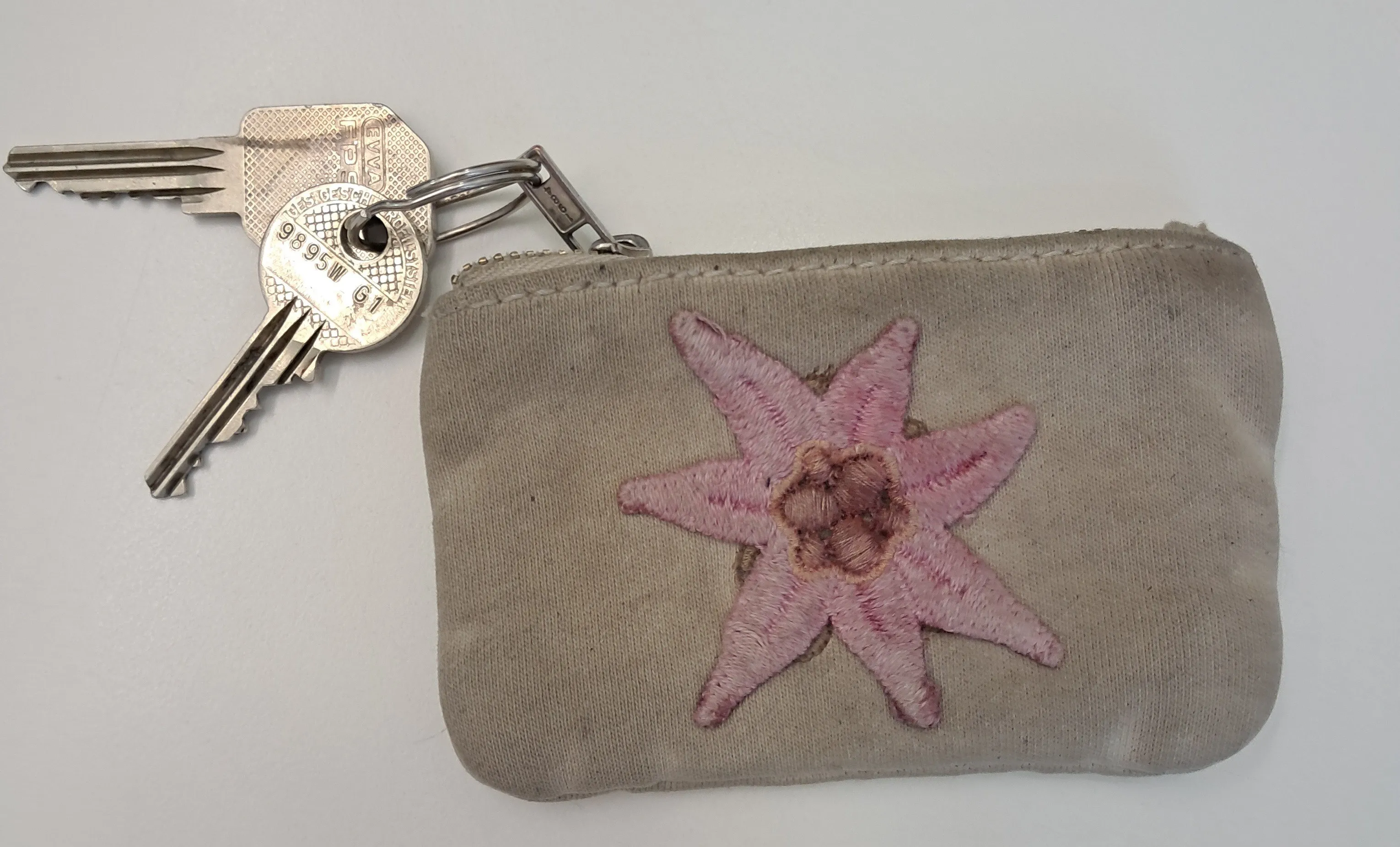 Ein kleiner grauer Beutel mit einem rosa Seestern-Design ist an einem silbernen Schlüssel befestigt.
