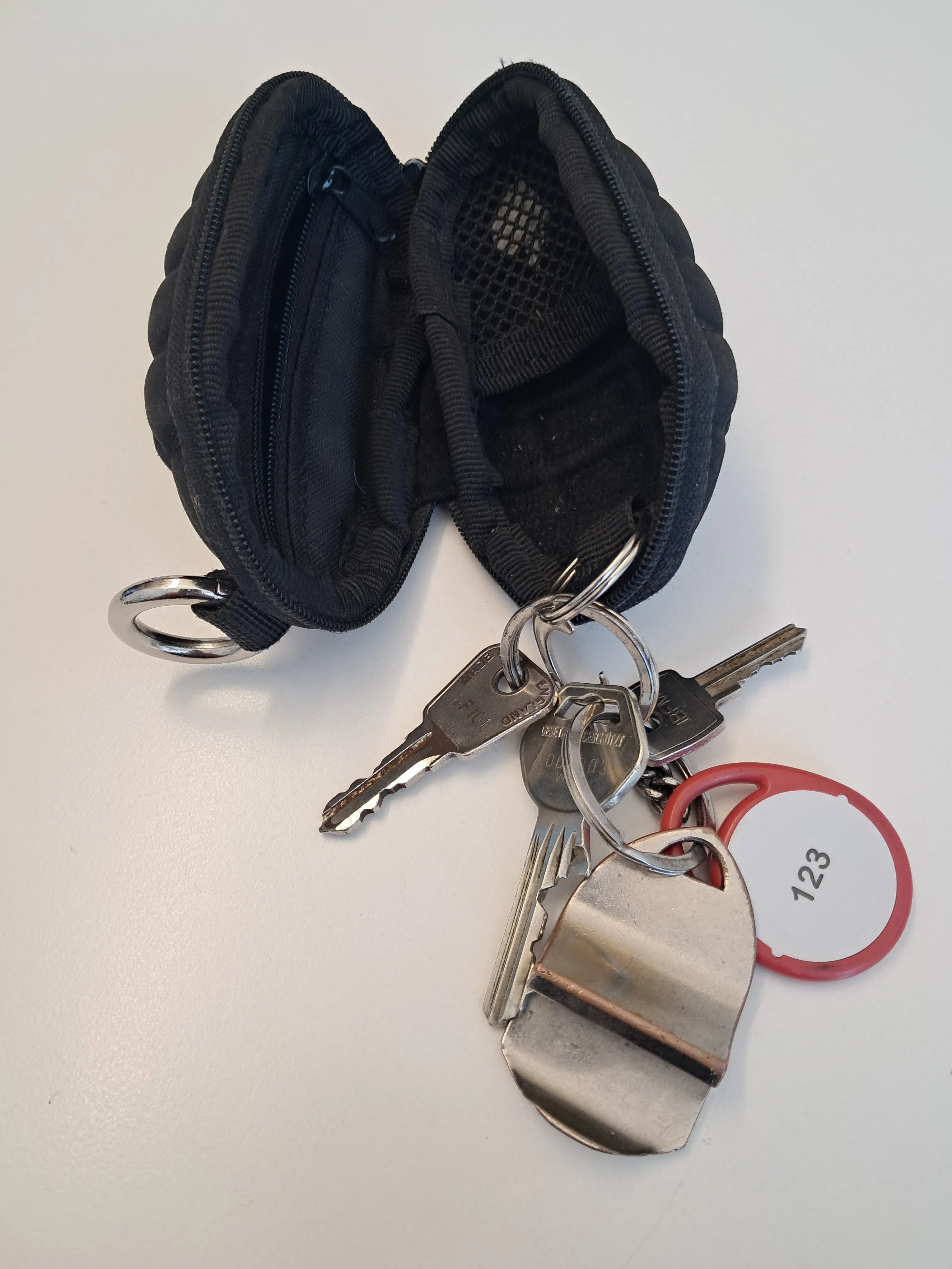 Ein Satz Schlüssel mit einem herzförmigen Schlüsselanhänger, einem roten Schlüsselanhänger und einem Nummernschild 123, zusammen mit einem schwarzen Schlüsselhalter auf einer weißen Oberfläche.