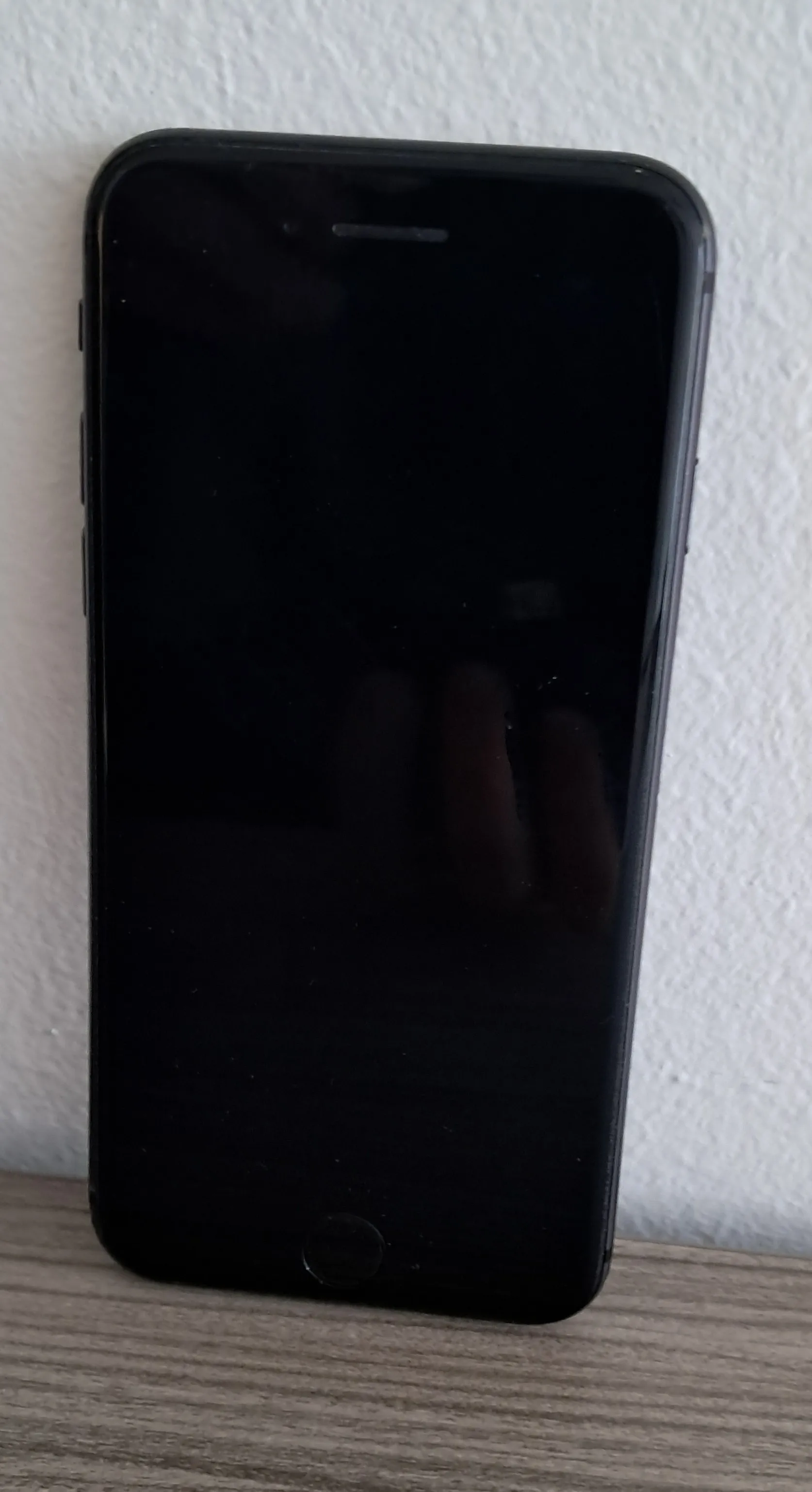 Ein Smartphone wird in einer Nahaufnahme gezeigt, der Bildschirm ist ausgeschaltet und zeigt einen dunklen Hintergrund mit einem schwachen Umriss einer Hand.
