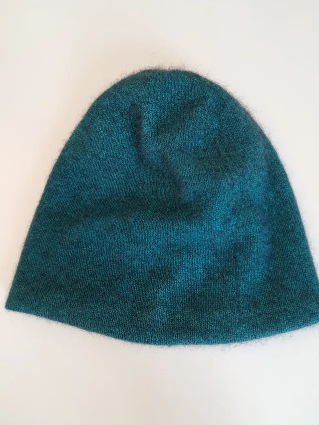 Ein gestrickter türkisblauer Beanie-Hut, der auf einem weißen Hintergrund präsentiert wird. Der Hut hat eine leicht strukturierte Oberfläche.