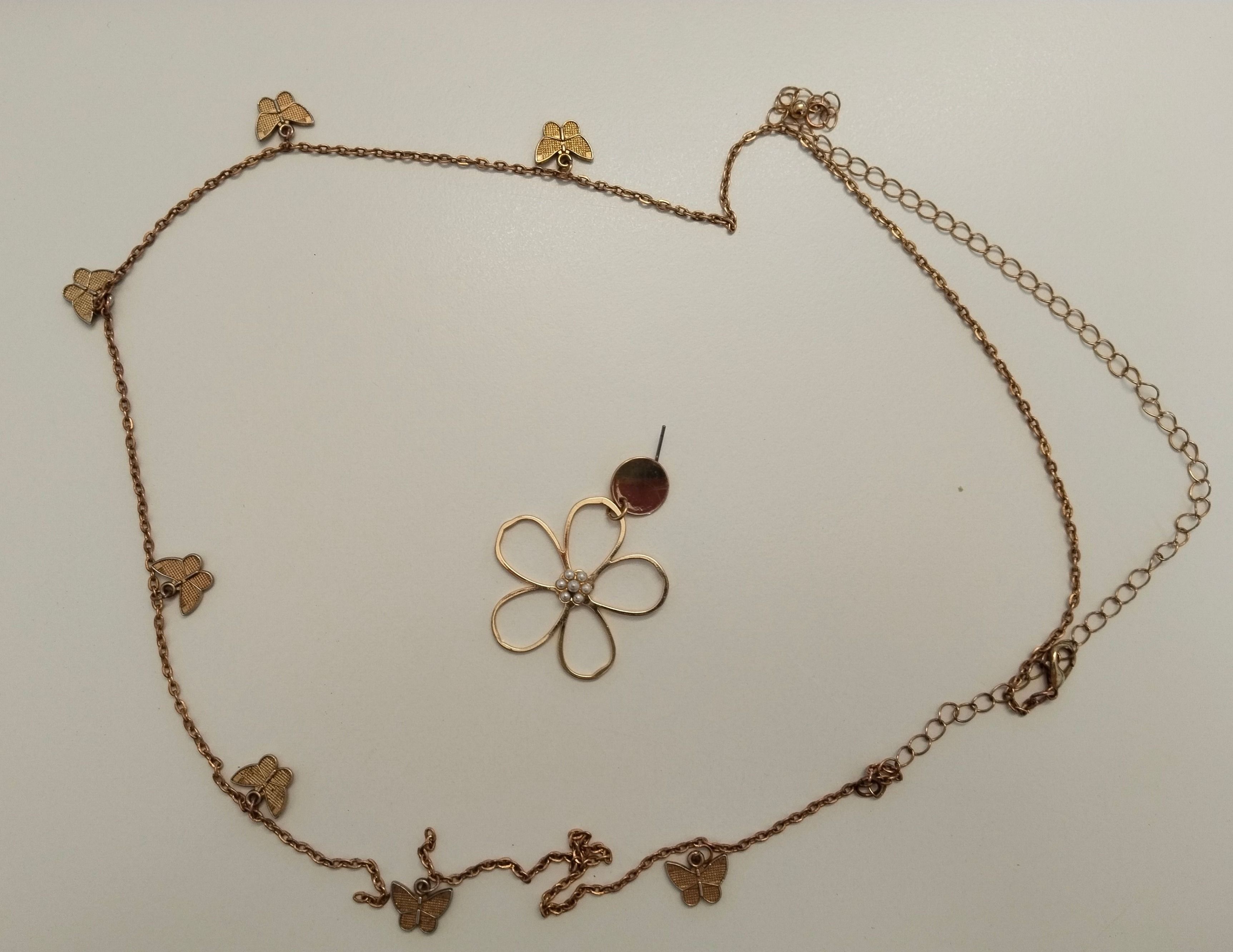 Eine goldfarbene Halskette mit einem Blumenanhänger und Schmetterlingsanhängern auf weißem Hintergrund.