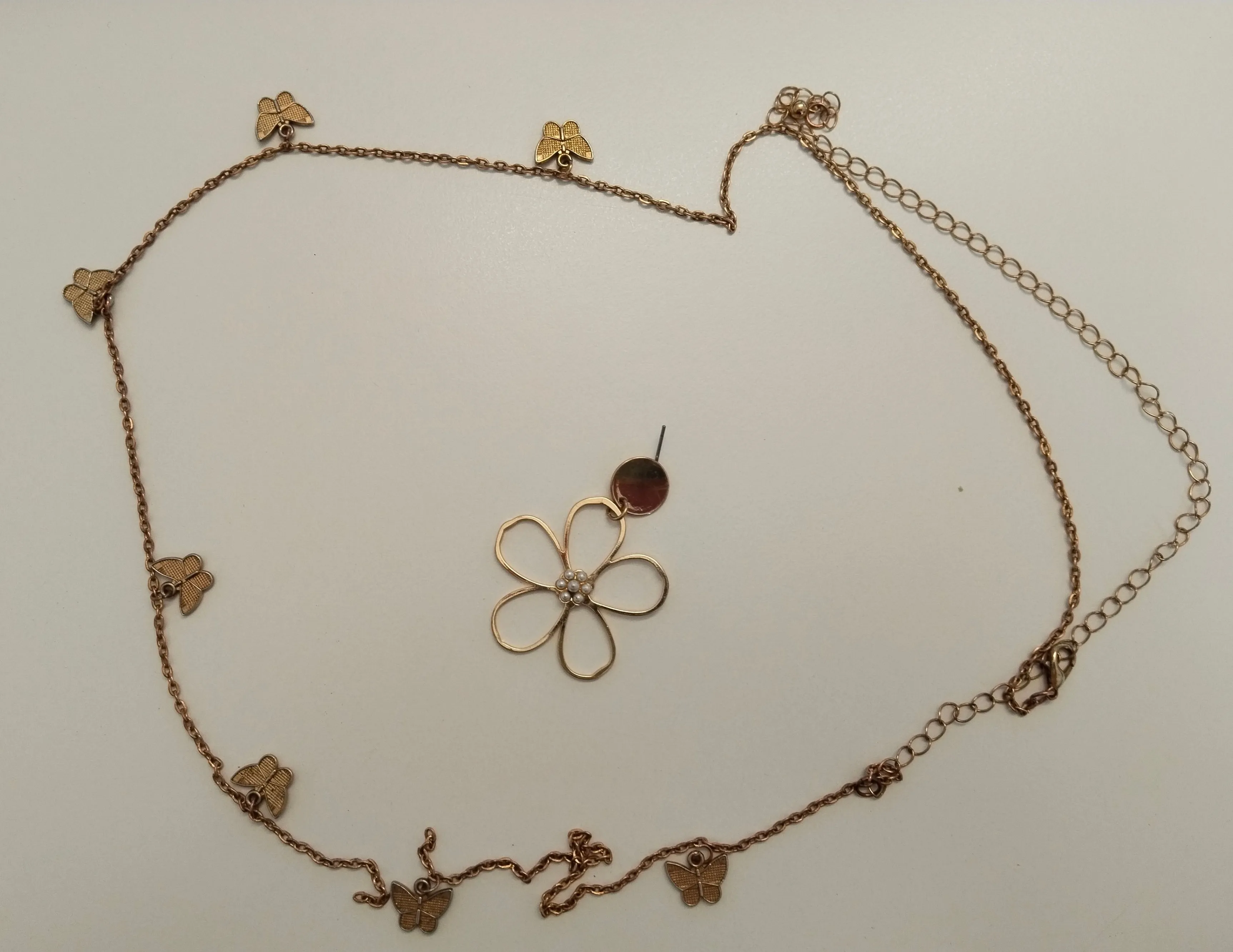 Eine goldfarbene Halskette mit einem Blumenanhänger und Schmetterlingsanhängern auf weißem Hintergrund.