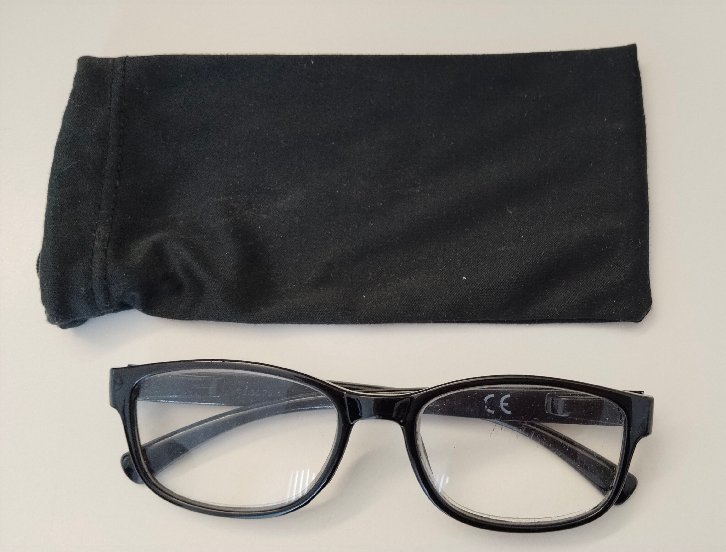 Ein Paar schwarzer Brille mit klaren Gläsern und einem schwarzen Etui auf einer weißen Oberfläche.
