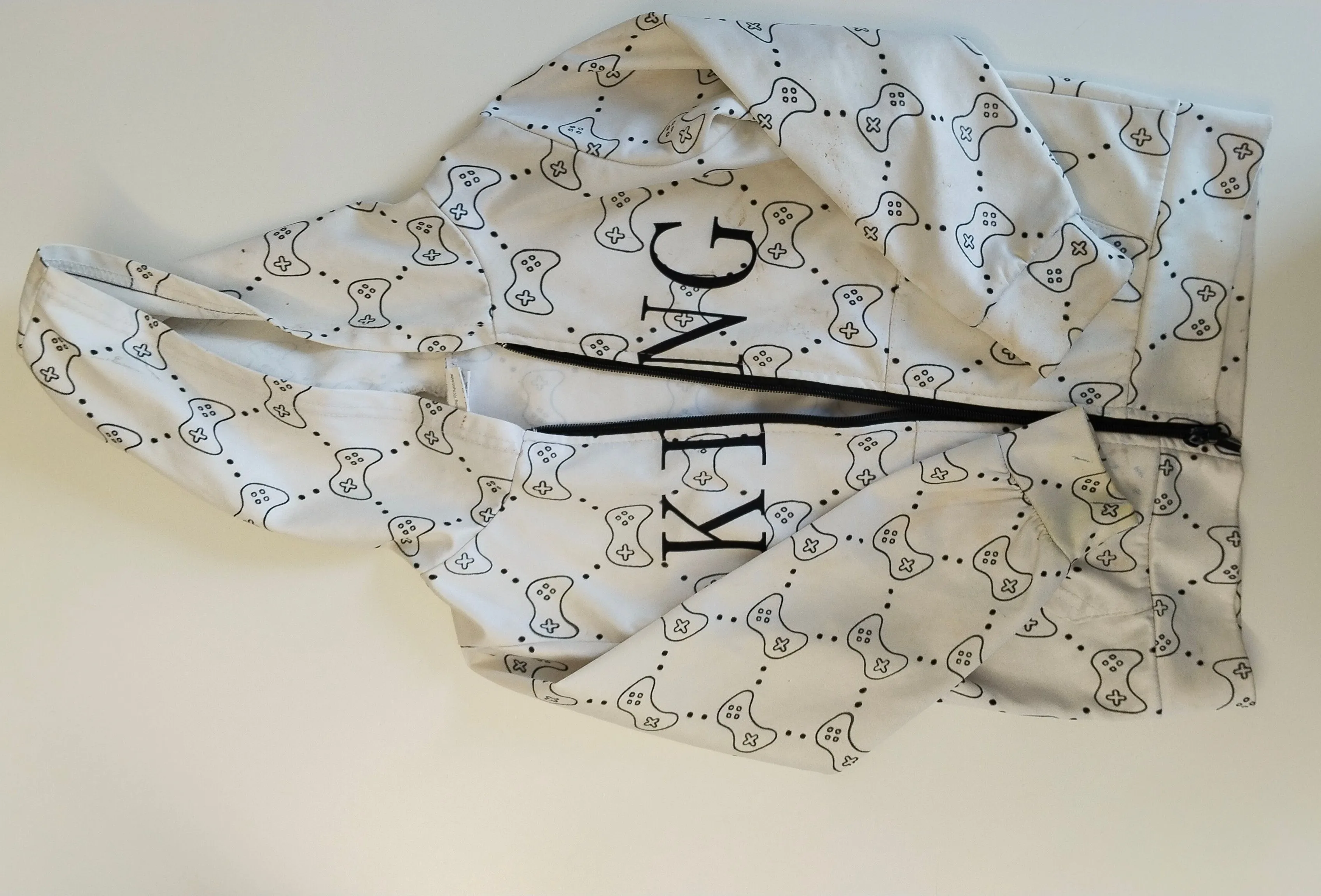 Ein weißes Kleidungsstück mit einem Gaming-Controller-Muster und dem Wort 'KING' in Schwarz gedruckt. Das Kleidungsstück ist gefaltet und scheint eine Kapuzenjacke zu sein.