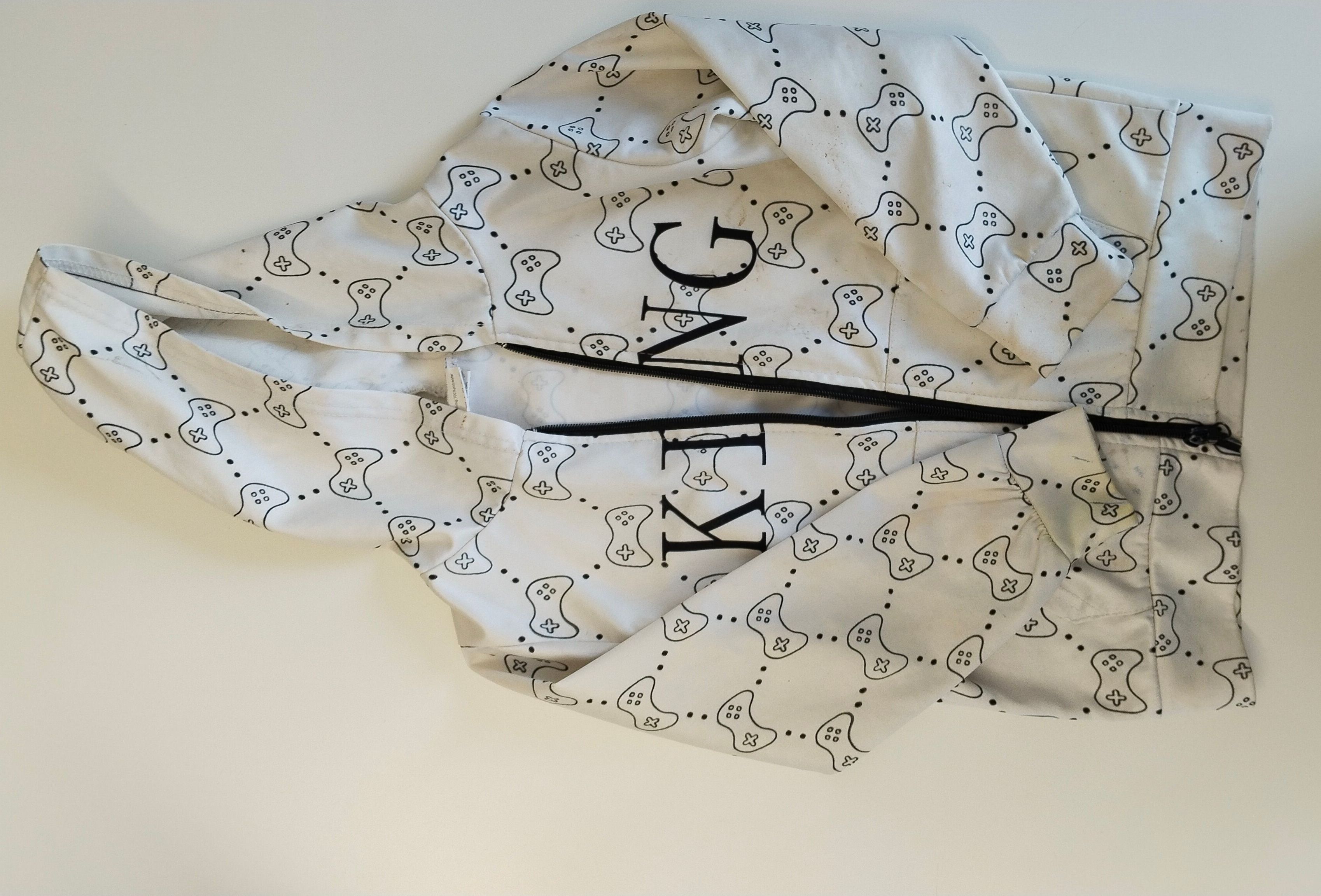Ein weißes Kleidungsstück mit einem Gaming-Controller-Muster und dem Wort 'KING' in Schwarz gedruckt. Das Kleidungsstück ist gefaltet und scheint eine Kapuzenjacke zu sein.