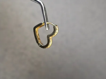 Eine Nahaufnahme eines herzförmigen Anhängers aus Silber und Gold, der an einem Haken hängt.