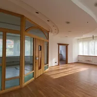 Ein leerer Raum mit Holzböden, Glaswänden und einer gewölbten Decke. Der Raum hat eine Tür und Fenster mit weißen Vorhängen. Der Raum ist gut beleuchtet.