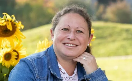 Eine Frau lächelt und posiert für ein Foto mit einem Sonnenblumenfeld im Hintergrund.