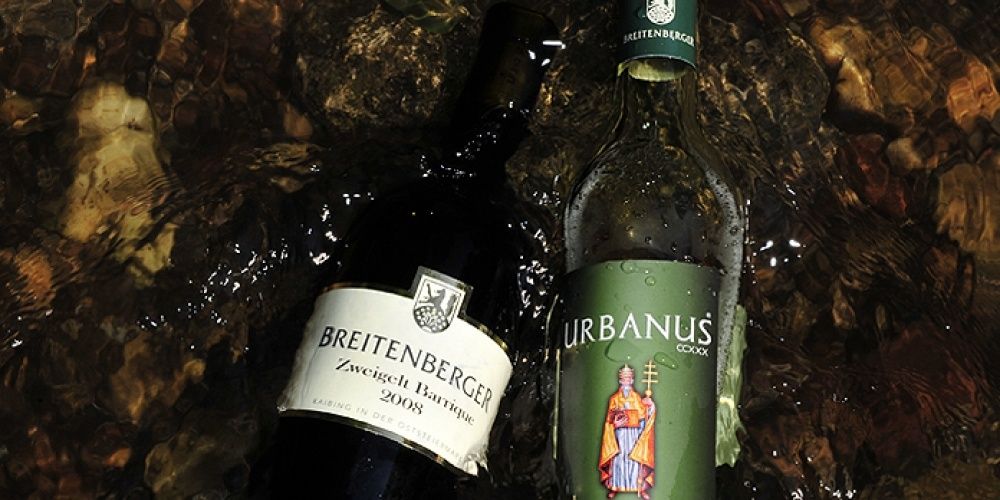 Zwei Weinflaschen im Wasser, eine ist Breitenberger Zweigelt Barrrique 2008 und die andere ist Urbanus CCCX mit einem Etikett, das einen Mann mit einem Kreuz zeigt.