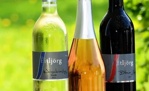Drei Weinflaschen sind aufgereiht. Die linke Flasche ist grün, die mittlere golden und die rechte dunkel. Die Etiketten zeigen den Namen des Weinproduzenten, Ettljorg, und das Jahrgangsjahr an.